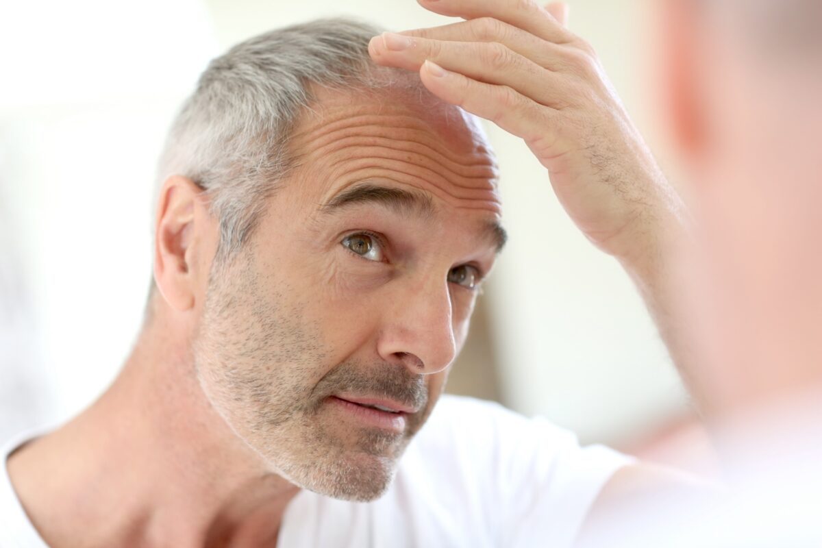 Man with graying hair inspecting thinning hairline in mirror